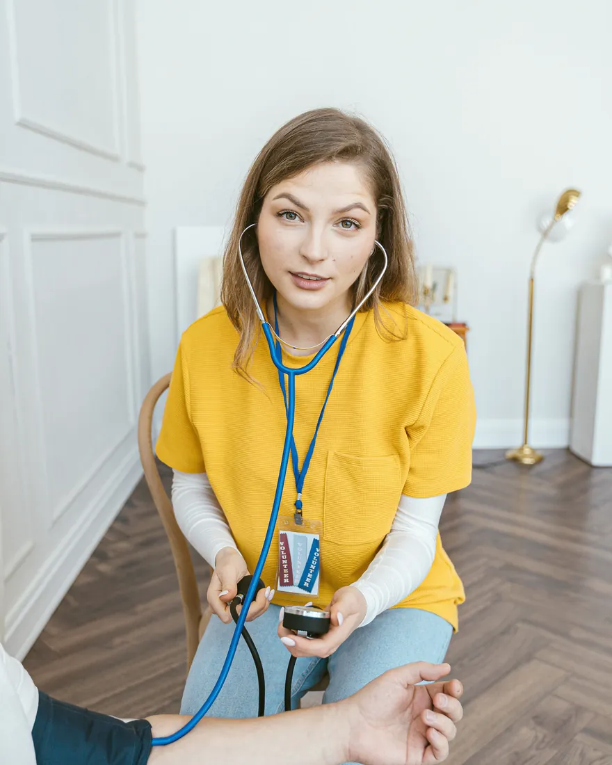 Eine Pflegekraft mit Stethoskop und Blutdruckmessgerät sitzt bei einem Patienten.